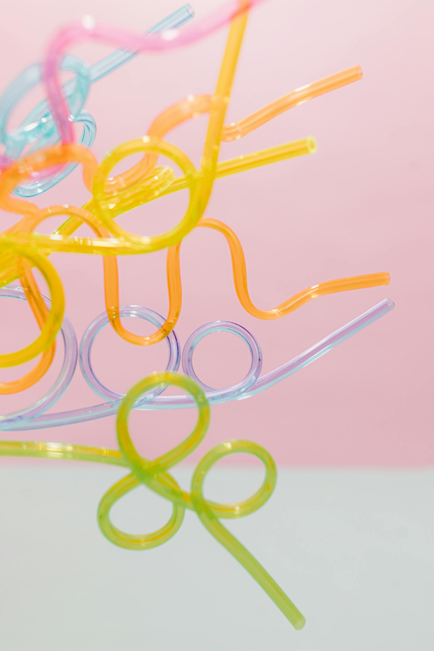 Vibrant plastic drinking straws with loops set against a soft pink and white background, perfect for party themes.